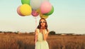 Cute young woman with bunch of colorful balloons outdoors in field Royalty Free Stock Photo