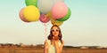 Cute young woman with bunch of colorful balloons outdoors in field Royalty Free Stock Photo