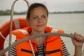 Cute young woman captain in the life jacket at the helm of the yacht