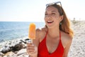Cute young woman eating an orange popsicle on the beach on summer Royalty Free Stock Photo