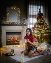 Cute, young woman by fireplace with a Christmas tree,Family sitting on a floor. woman near christmas tree Royalty Free Stock Photo