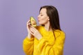 Cute young woman in fur sweater keeping eyes closed holding, kissing half of fresh ripe avocado isolated on violet Royalty Free Stock Photo