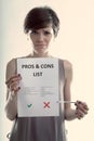 Cute young woman holding up a Pros and Cons list