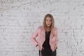 Cute young woman on leather jacket. Fashion model in pink leather jacket. Posing near white brick wall.