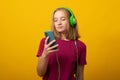 Cute young woman listens music in headphones holds mobile phone chooses song from playlist dressed in casual t-shirt Royalty Free Stock Photo