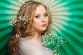 Cute young woman with long healthy blonde curly hair, make up and flowers on green background Royalty Free Stock Photo