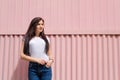 Cute young woman with long straight dark hair in white t-shirt and blue jeans on pink background. Female standing tucked hand Royalty Free Stock Photo