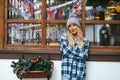 Cute young woman plaid shirt, pom pom hat on a background of wooden shale decorated evergreen tree. Christmas moody portrait Royalty Free Stock Photo