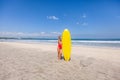 Cute young woman in red swimsuit with surfboard alone on the beach with waves