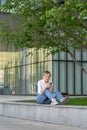 Cute young woman sitting on bench in spring park under tree outdoors resting using smartphone Royalty Free Stock Photo