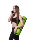 Cute young woman in sportswear with green mat ready for workout. Smiling and talking on the phone. Isolated on white background. Royalty Free Stock Photo