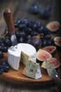 Cuted blue cheese, fresh fig halfs and grapes on rustic wooden plate. Moody scene with selective focus