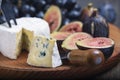 Cuted blue cheese, fresh fig halfs and grapes on rustic wooden plate. Moody scene with selective focus