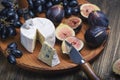 Cuted blue cheese, fresh fig halfs and grapes on rustic wooden plate. Moody scene with selective focus