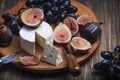 Cuted blue cheese, fresh fig halfs and grapes on rustic wooden plate. Moody scene with selective focus