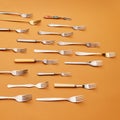 Cutlery. Flat lay of variety of stainless steel, silver and golden forks symmetrically arranged against orange studio