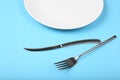 Cutlery for food on a blue background. A fork and knife with a white plate, close up Royalty Free Stock Photo