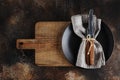 Cutlery on the plate on dark brown background. Fork and table-knife with wooden handles on linen napkin and wooden board