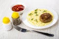 Cutlet with mashed potato in plate, salt, pepper, bowl with lecho, fork on table