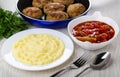 Cutlets in frying pan, lecho, dill, mashed potato in plate, fork, spoon on table