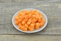 Cuts cubes of carrot in white plate on wooden table Royalty Free Stock Photo