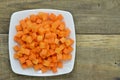 Cuts cubes of carrot in white plate on wooden table Royalty Free Stock Photo