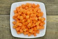 Cuts cubes of carrot in white plate on wooden table, detail Royalty Free Stock Photo