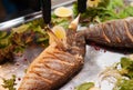 Cuts fried dorado fish on a large metal platter. Lettuce and lemon. Knife and fork. defocus