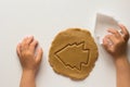 Cutted form of christmas tree on rolled out gingerbread dough by child hands on white background