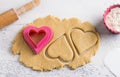 Cutted heart shaped dough cookies with cookie cutters, rolling pin and bowl of flour on a light blue tabletop, top view