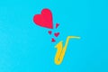 A cutted out of felt saxophone from which hearts flew out, on a blue background. Flat lay. International Jazz Day. Copy space