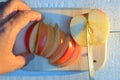 Cutting an apple with his hand with knife on cutting wooden cutting board on a white background at sunset