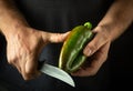 Cutting bell pepper with knife in chef hands. Concept on black background of cooking vegetable dish. Cutting green pepper