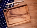 Cutting board on blue fabric polka dots or napkin and knive, fork on rustic wood background.