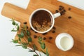 Cutting board with cup of fresh coffee, milk, coffee beans and plant branch on white background Royalty Free Stock Photo