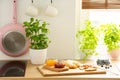 Cutting board with French croissants and fruit jams and natural herbs in a bright kitchen interior with a white wall