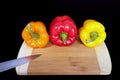 Cutting board with paprika and knife. Three home peppers on black background.