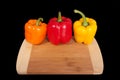 Cutting board with paprika. Three home peppers on black background.