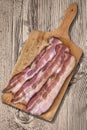 Bacon Rashers On Wooden Cutting Board Set On Old Knotted Rough Pine Wood Table Surface Royalty Free Stock Photo
