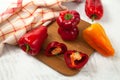 Cutting board with several whole and halves of red and yellow bell pepper and red kitchen towel on white wooden background Royalty Free Stock Photo