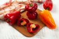 Cutting board with several whole and halves of red and yellow bell pepper and red kitchen towel on white wooden background Royalty Free Stock Photo