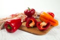 Cutting board with several whole and halves of red and yellow bell pepper and red kitchen towel on white wooden background Royalty Free Stock Photo