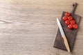 Cutting board with sharp knife and cherry tomatoes on wooden background, top view