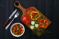 A cutting board with slices of tomatoes, cucumbers and peppers, a branch of dill, a fork and a knife, a plate of vegetable salad Royalty Free Stock Photo