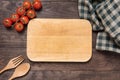 Cutting board with tomato, fork and spoon on wooden background Royalty Free Stock Photo