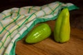 Cutting board with two green bell pepper and green kitchen towel on wooden background Royalty Free Stock Photo