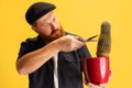 Comic portrait of stylish red-bearded man, barber in black cap having fun isolated over yellow background. Concept of