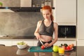 Athletic young red haired woman in the home kitchen prepares a vegetable centrifuged and a salad