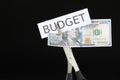 Cutting dollar banknote and paper with word Budget with scissors on black background, closeup Royalty Free Stock Photo