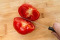 Cutting fresh red tomato with knife with sharp blade into two halves on a wooden kitchen board Royalty Free Stock Photo